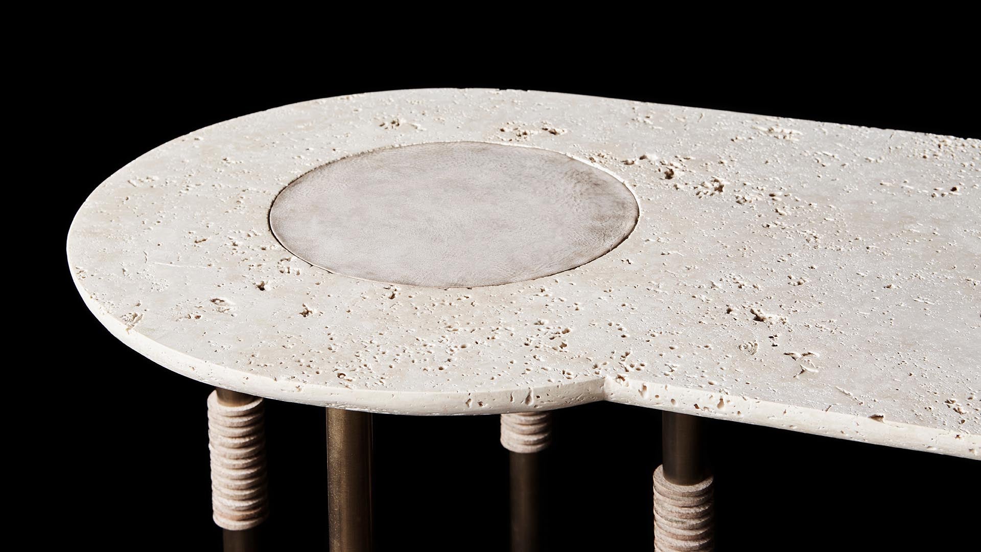 Close-up of an oval stone tabletop with a circular inlay, supported by vertical metal legs wrapped in light-colored rope.