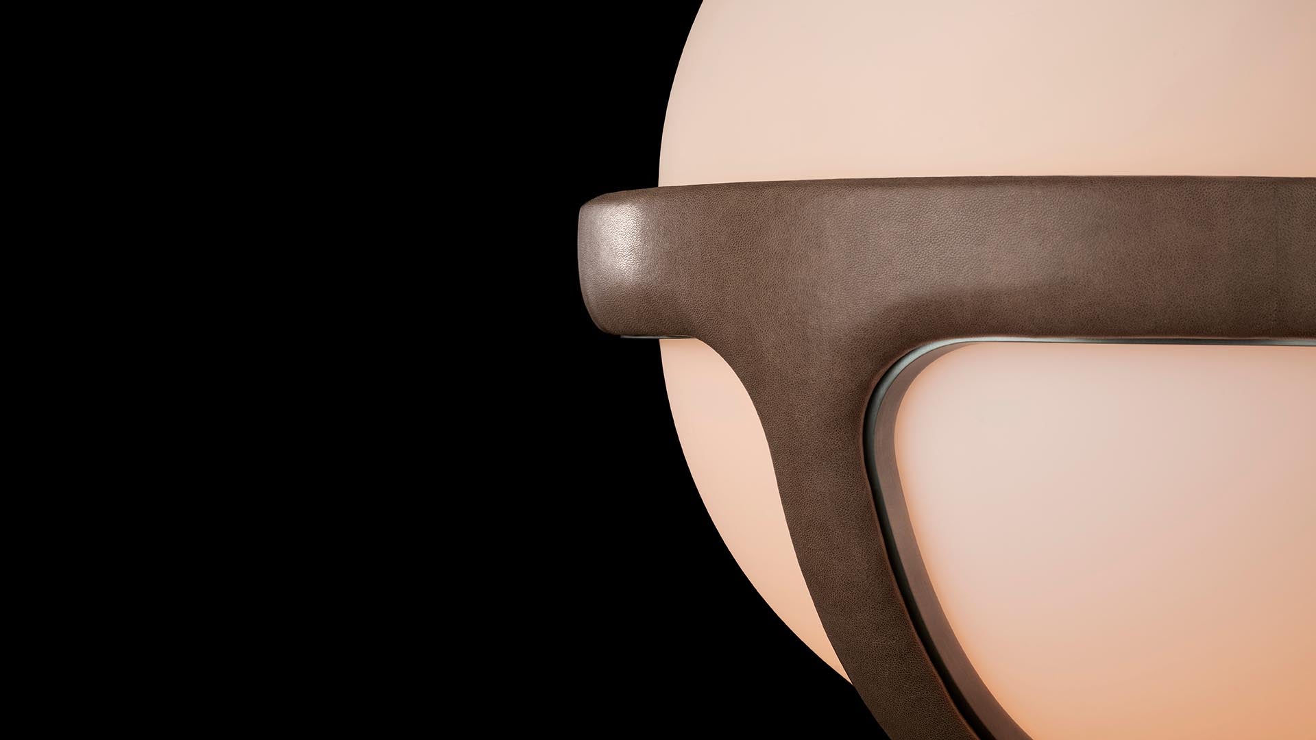 Close-up of a modern pendant light with matte brown metal frame and glowing round white glass shade on black background