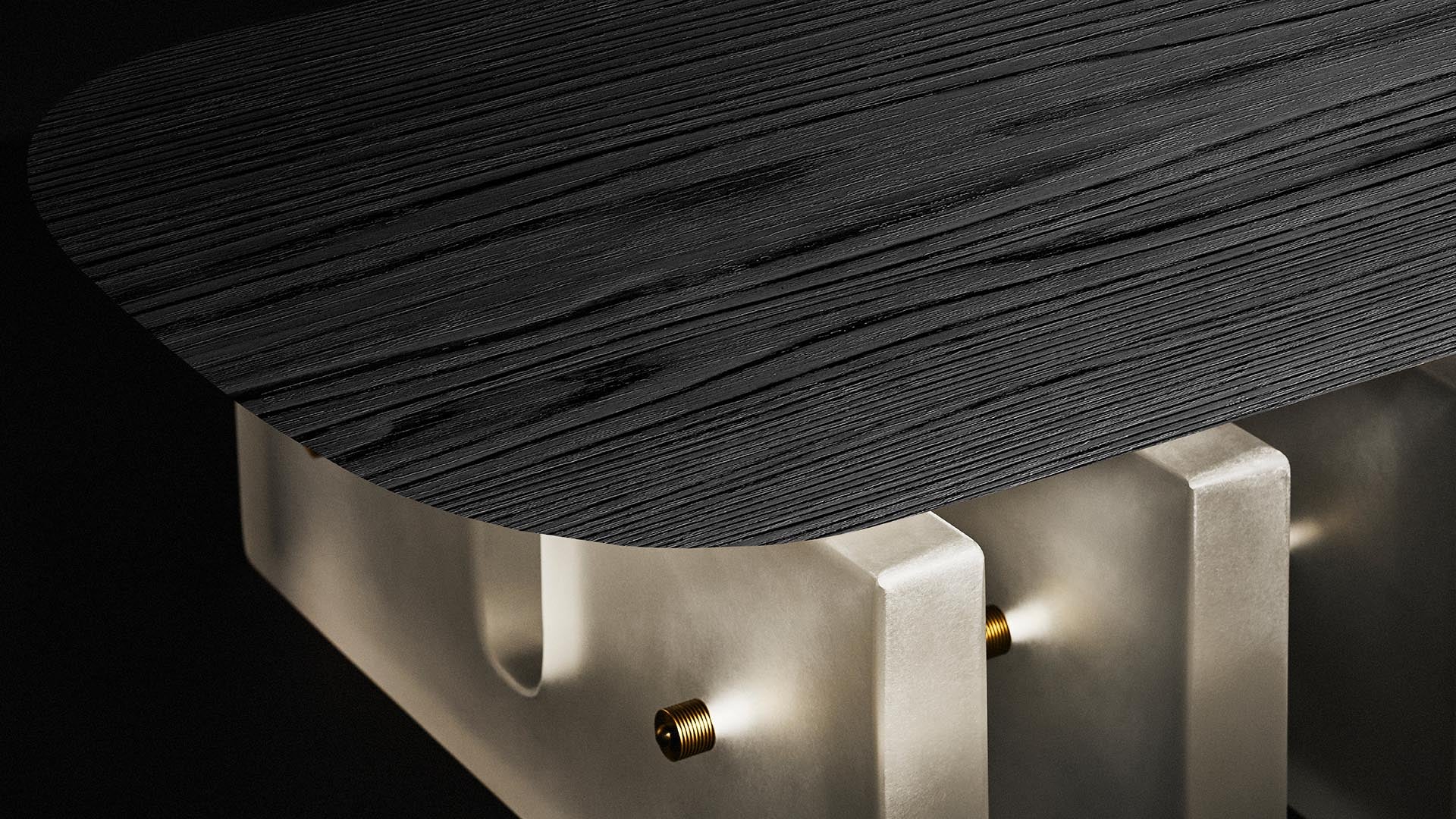 Close-up of a dark textured wooden table top with rounded edges supported by frosted glass legs and metallic connectors