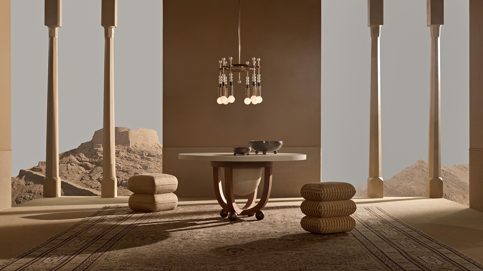 Minimalist interior with round stone table, hanging light fixture, textured cushions, and tall columns overlooking a desert landscape