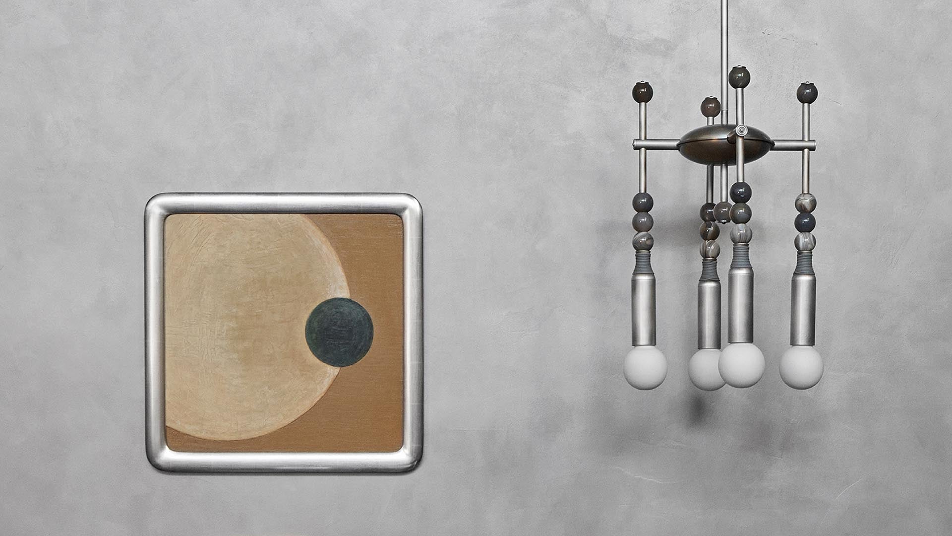 Abstract wall art with beige and dark circular shapes next to a modern metallic mobile with spherical elements on gray wall