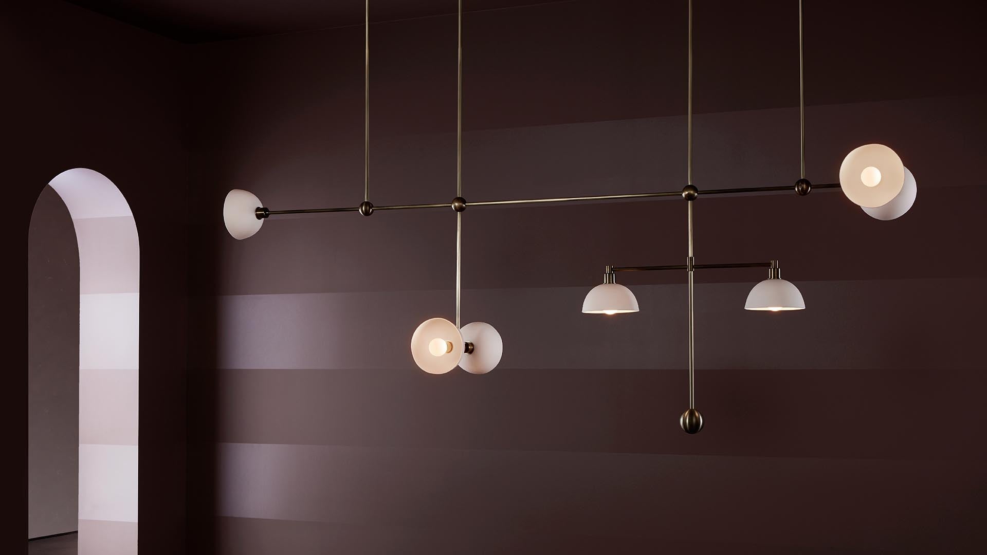 Minimalist modern chandelier with six round white lamps hanging against a striped dark brown wall and arched doorway.