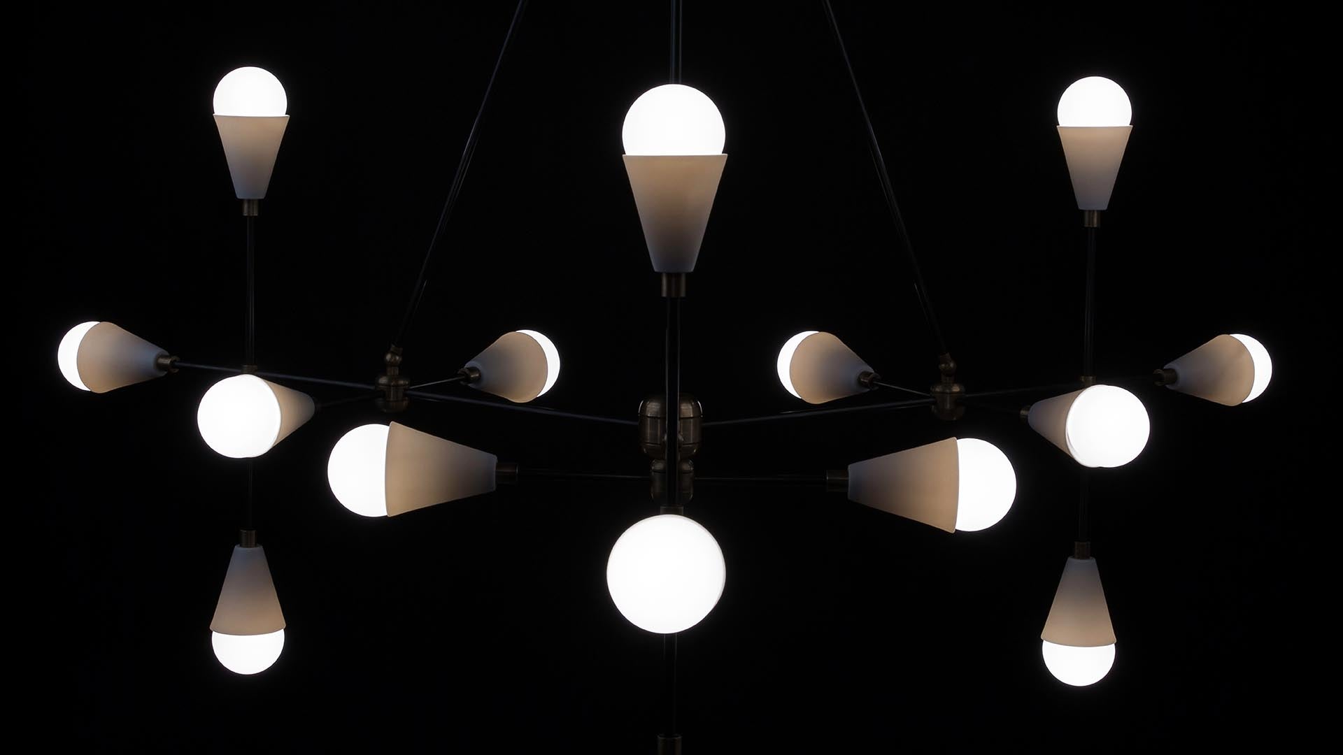 Close-up of a modern black metal chandelier with multiple white conical light bulbs against a dark background