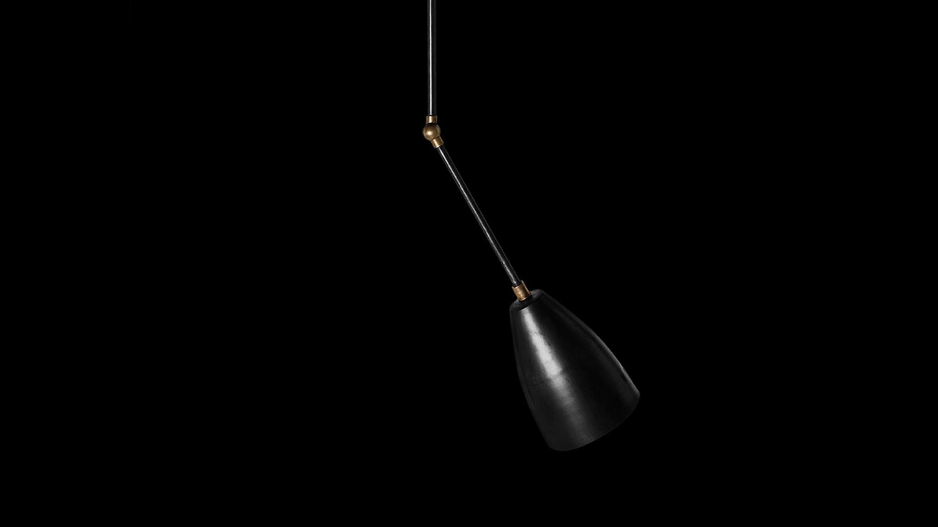 Minimalist black pendant light with angled arm and brass accent, suspended against a black background