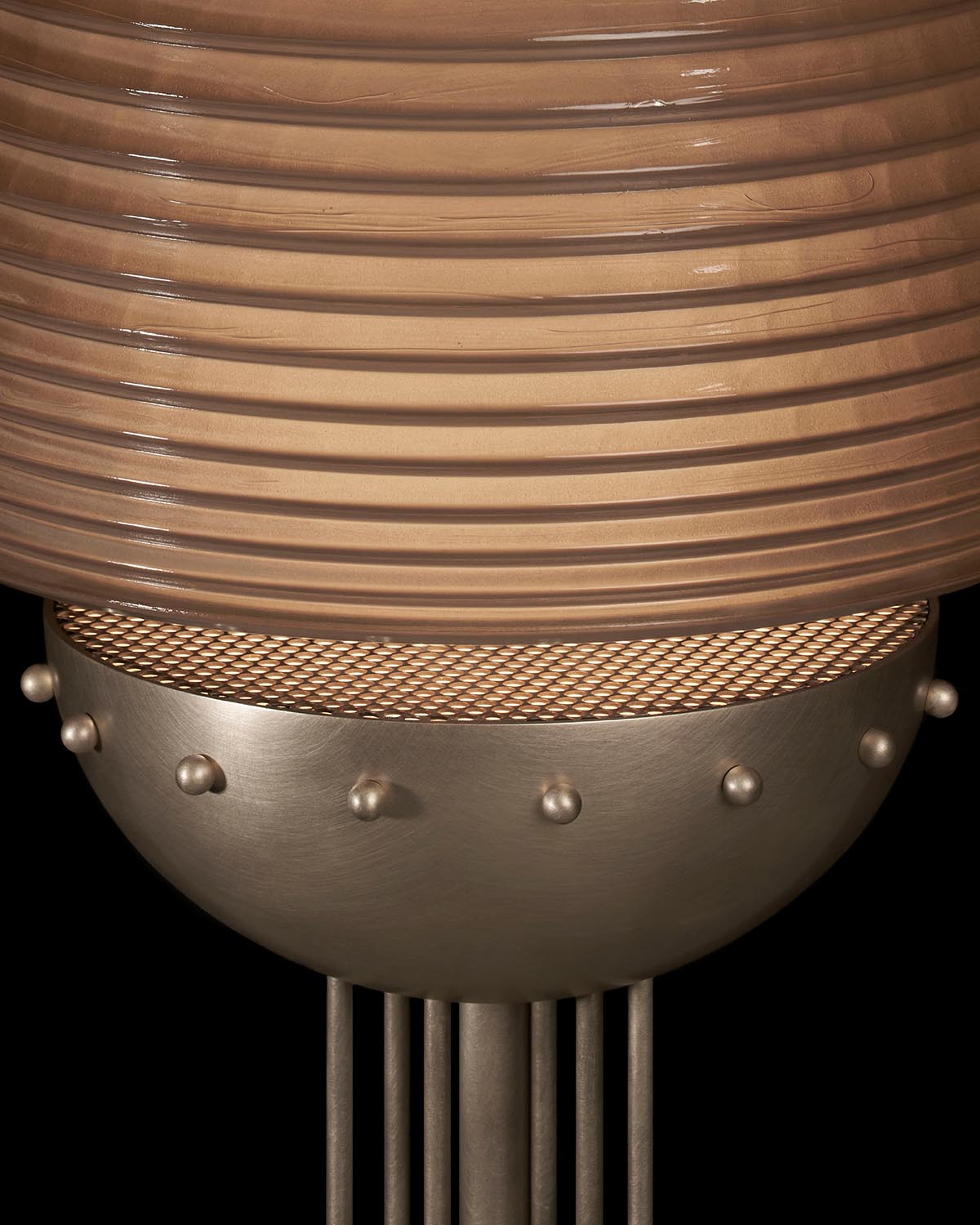 Close-up of textured brown glass lampshade and metallic base with patterned mesh and small round studs against black background