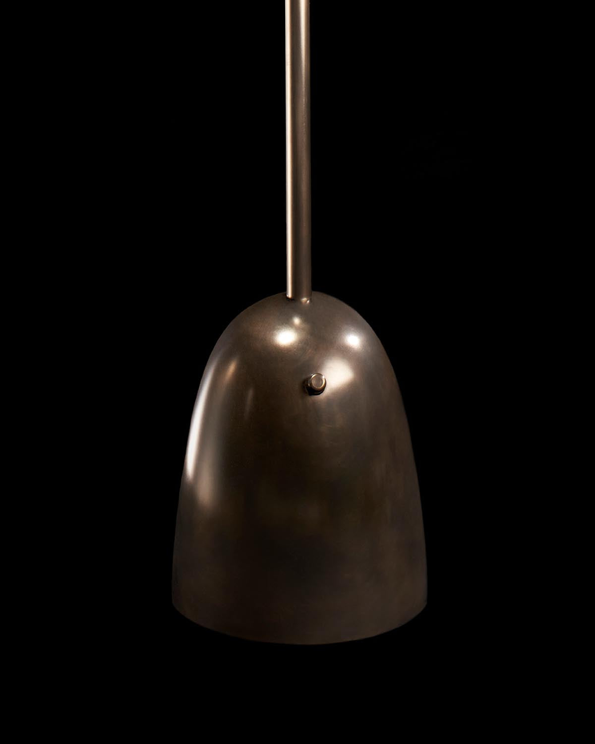 Close-up of metallic floor lamp shade with smooth dark bronze finish and cylindrical rod against black background