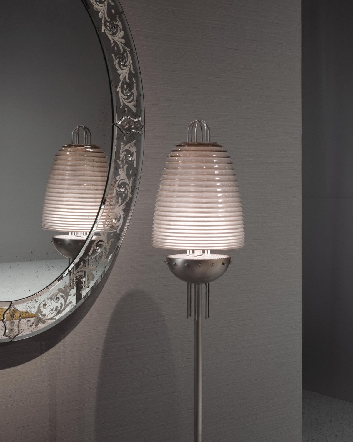 Modern floor lamp with ribbed frosted glass shade and metal base reflected in an ornate round mirror on gray wall