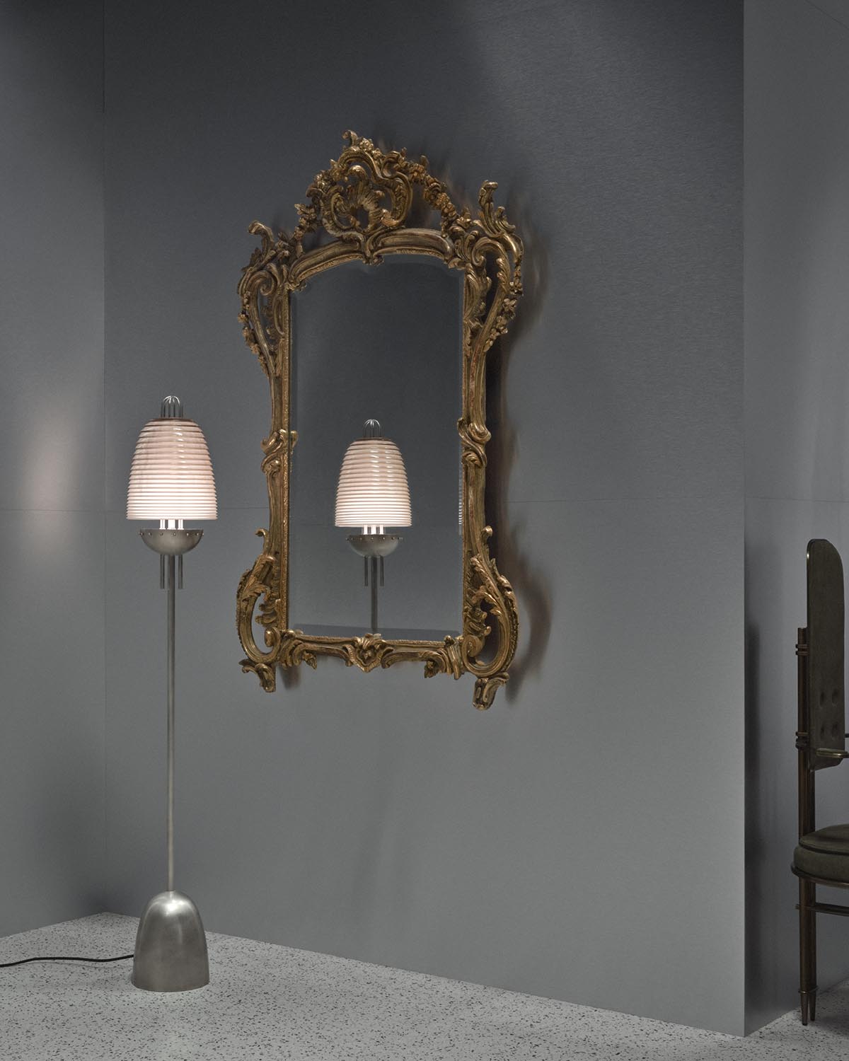 Modern floor lamp with ribbed white shade and sleek metallic base reflected in ornate gold-framed mirror on gray wall