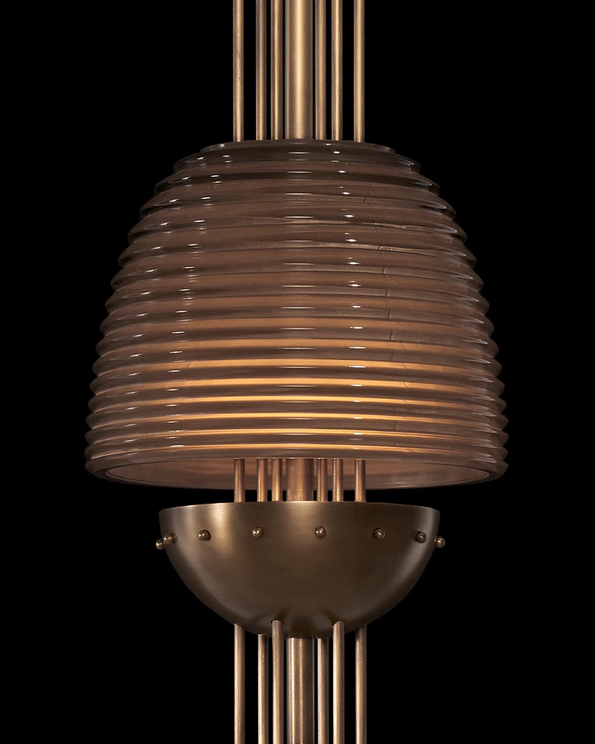 Close-up of SIGNAL X pendant light with layered ribbed glass shade and brass metal accents against a black background