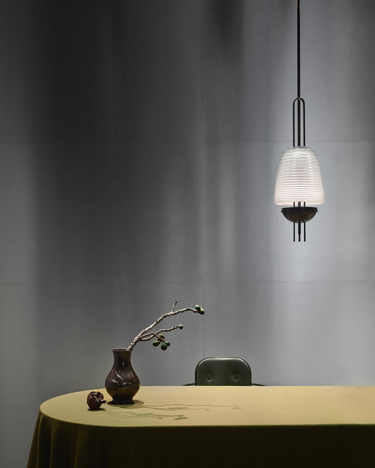 Minimalist interior featuring a SIGNAL X pendant light above an olive-green table with a dark vase and dried branch against a gray wall