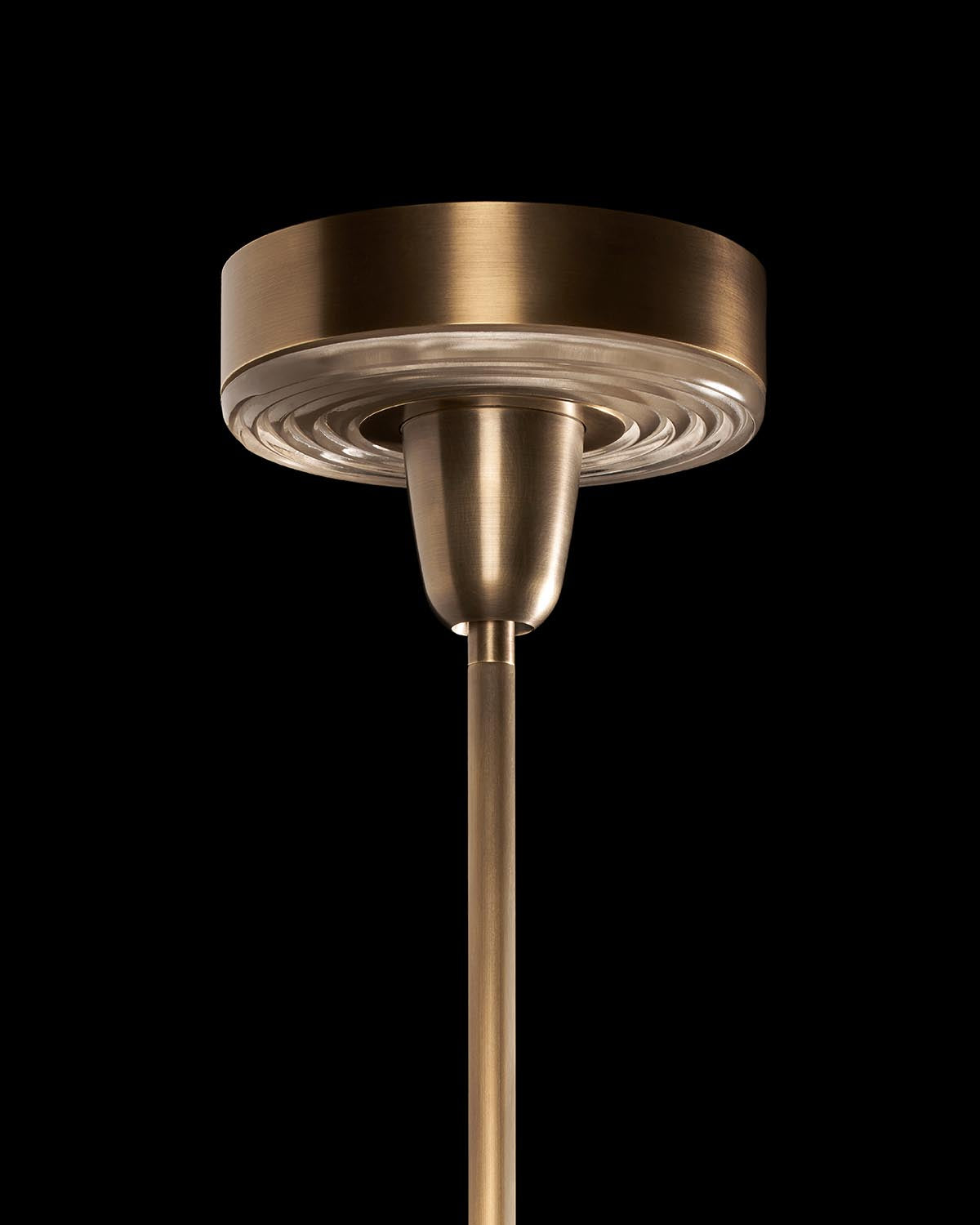 Close-up of a brushed brass ceiling mount and rod of a pendant light against a black background