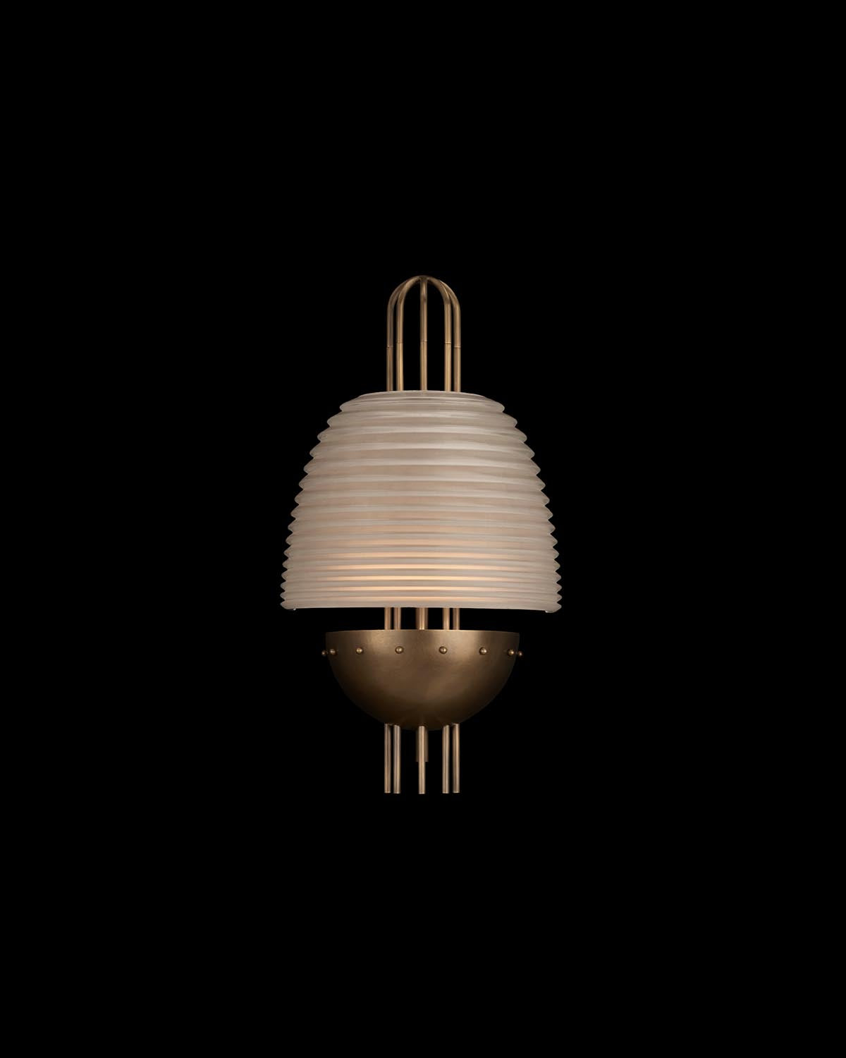 Modern wall sconce with ribbed glass shade and brass-toned metal base on a black background