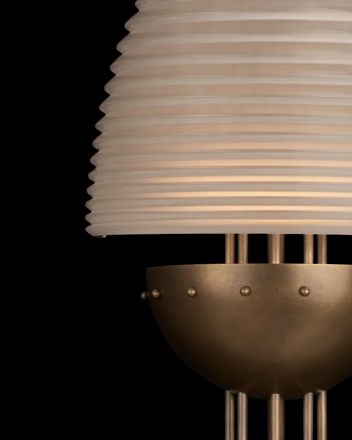 Close-up of modern sconce with ribbed white shade and brushed brass dome base against a black background