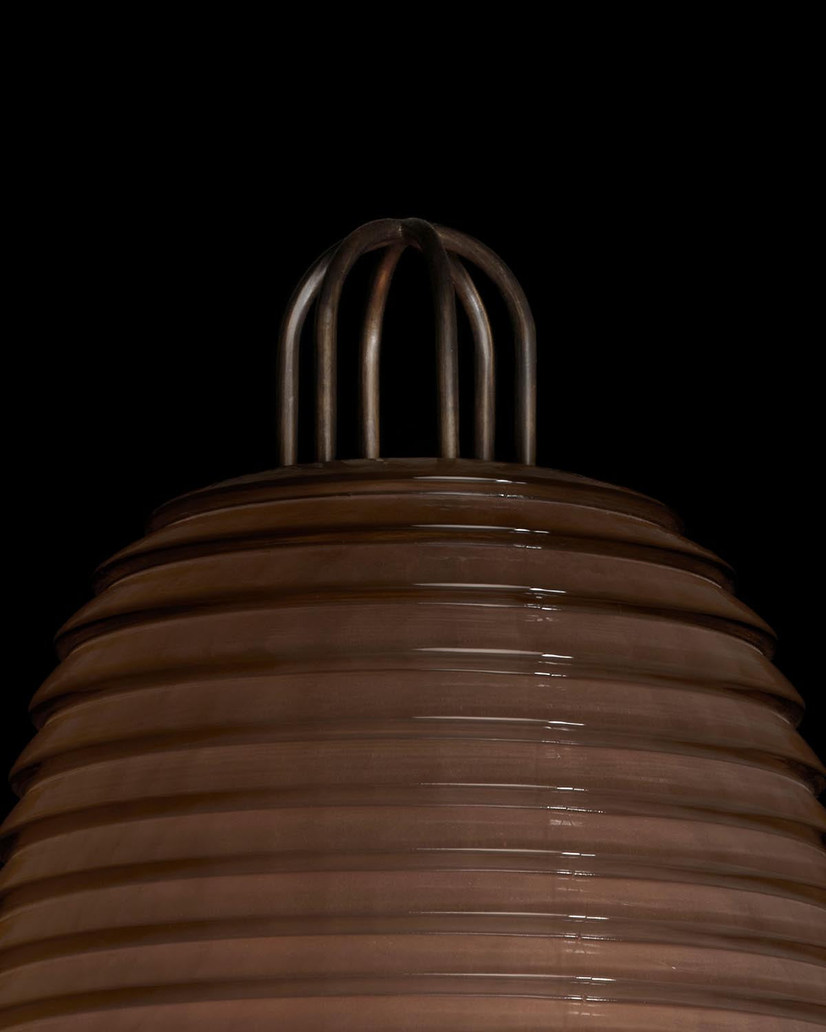 Close-up of a ribbed brown ceramic sconce with metal loop detail on top against a black background