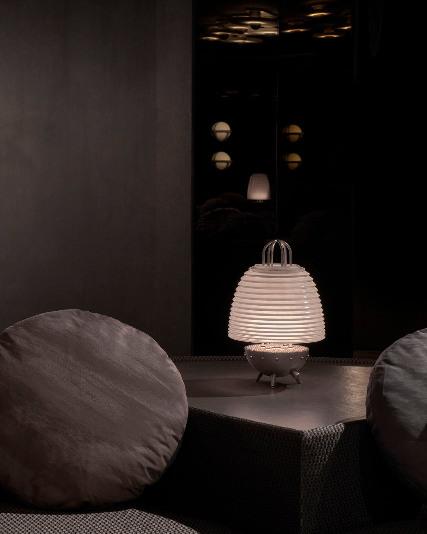 Modern white ribbed table lamp with rounded base on a dark textured surface between two round cushions