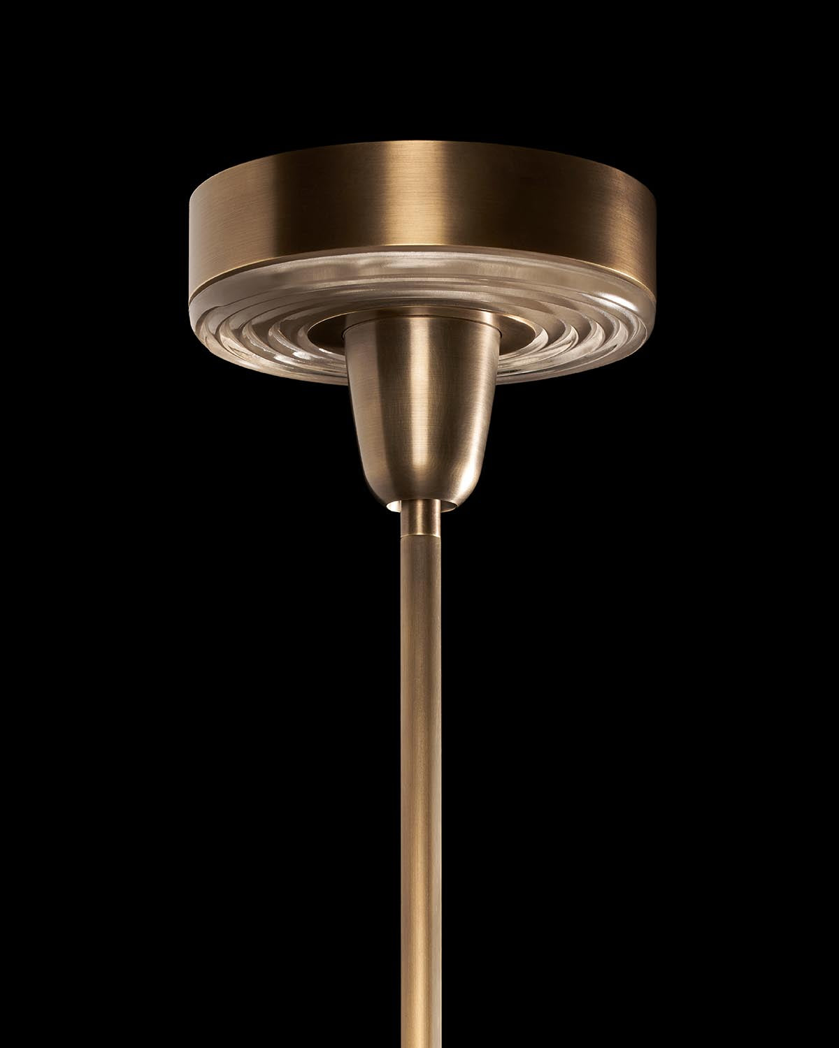 Close-up of brass pendant light ceiling mount with ribbed glass diffuser against a black background