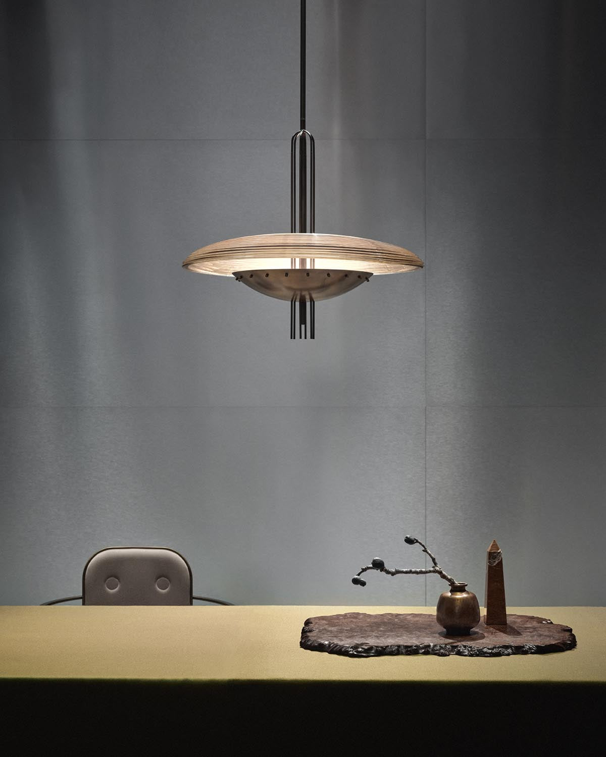Suspended modern pendant light with layered circular wooden shade above minimalist table setting with vase and sculpture