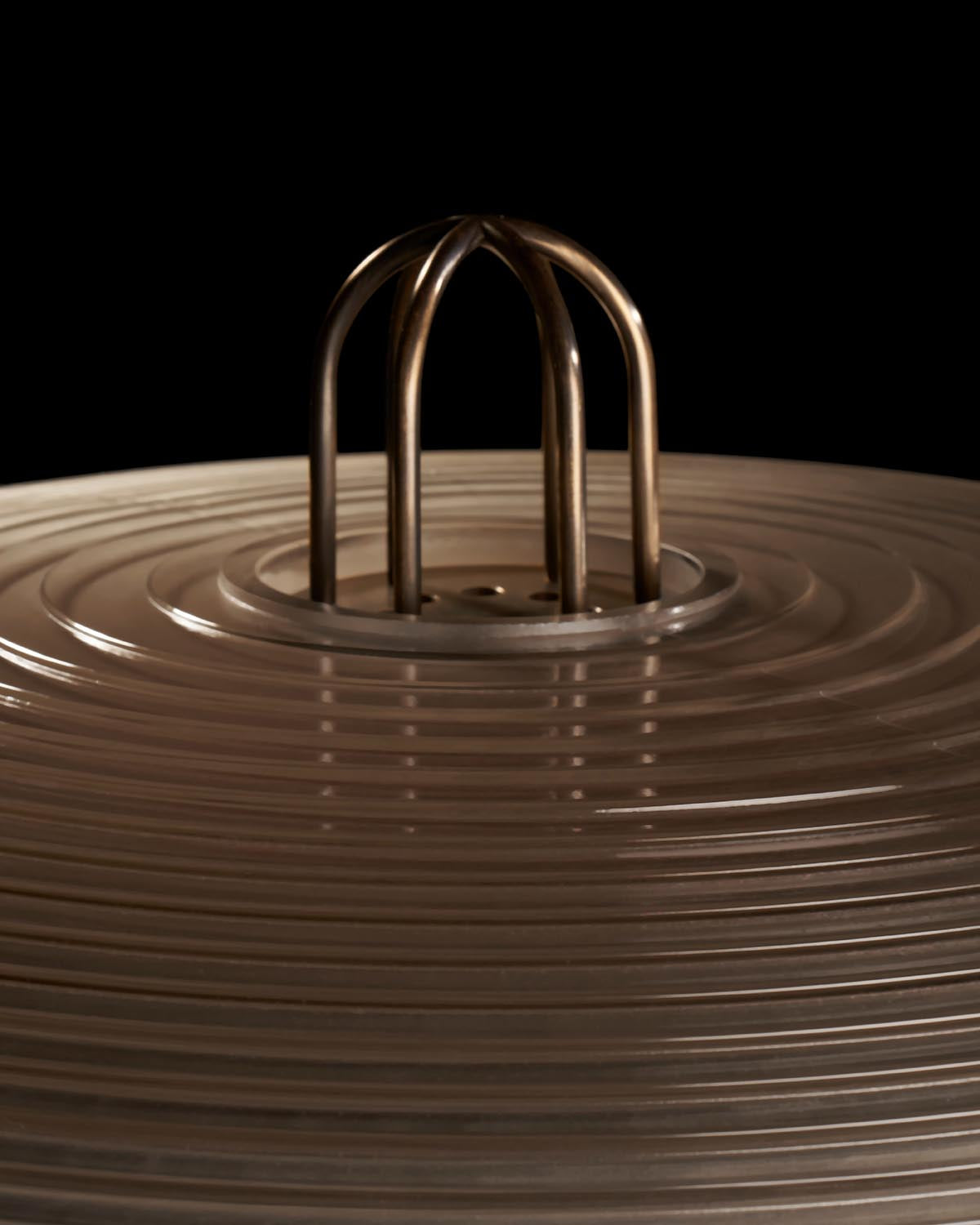 Close-up of circular ribbed glass lampshade with bronze curved metal handle against a black background