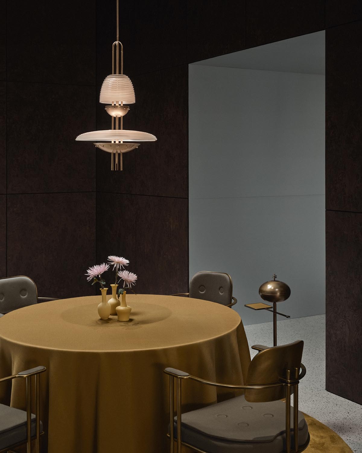 Modern pendant light with layered circular shades hanging above round table with gold cloth and beige chairs