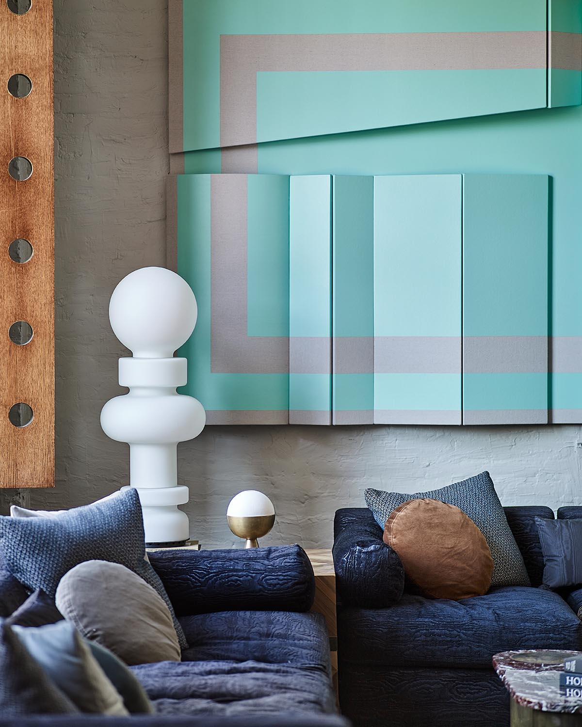 Contemporary living room with navy blue sofa, textured cushions, abstract turquoise wall art, and white sculptural lamp on wooden table