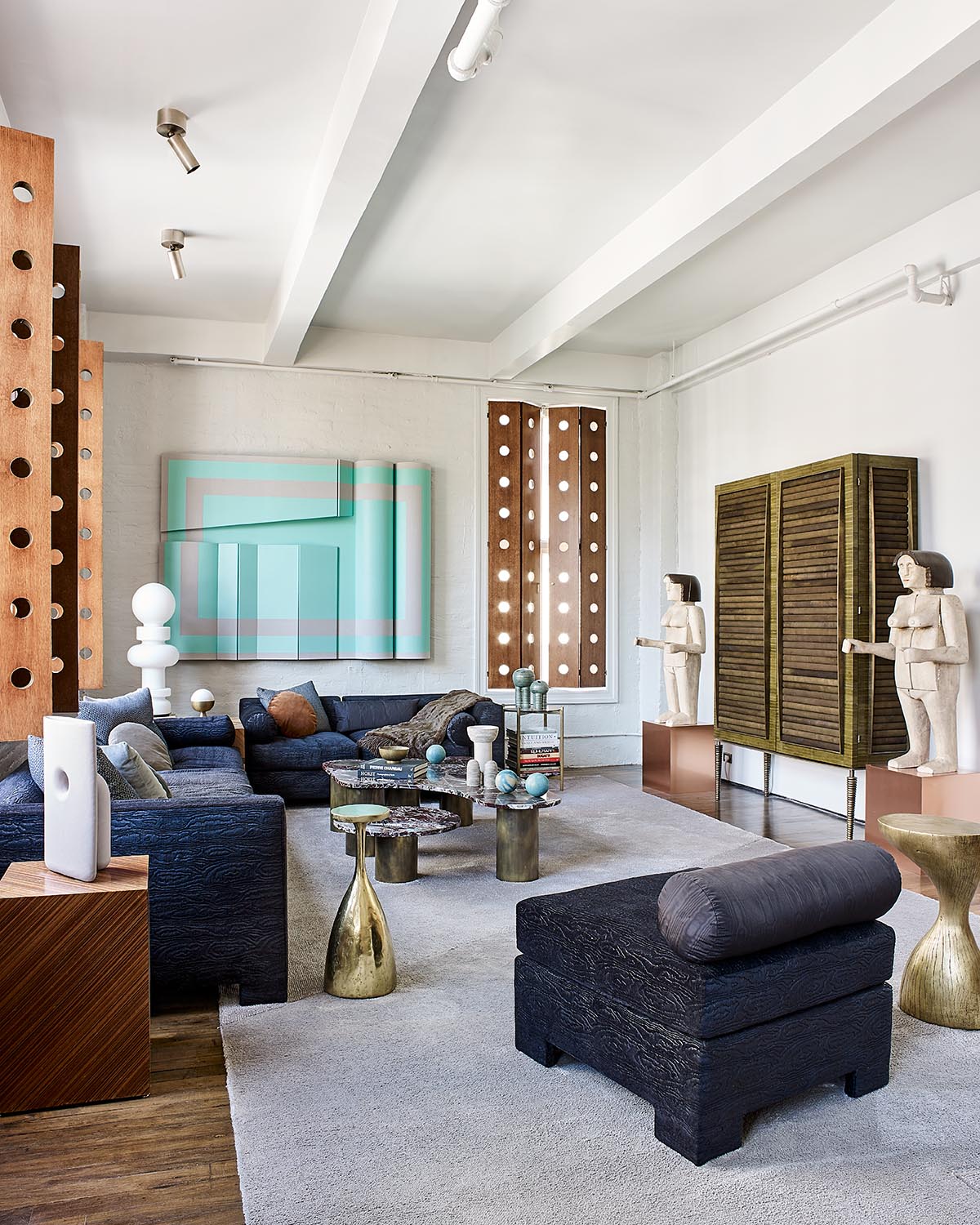 Contemporary living room with dark textured seating, brass side tables, sculptural decor, and abstract wall art on white walls
