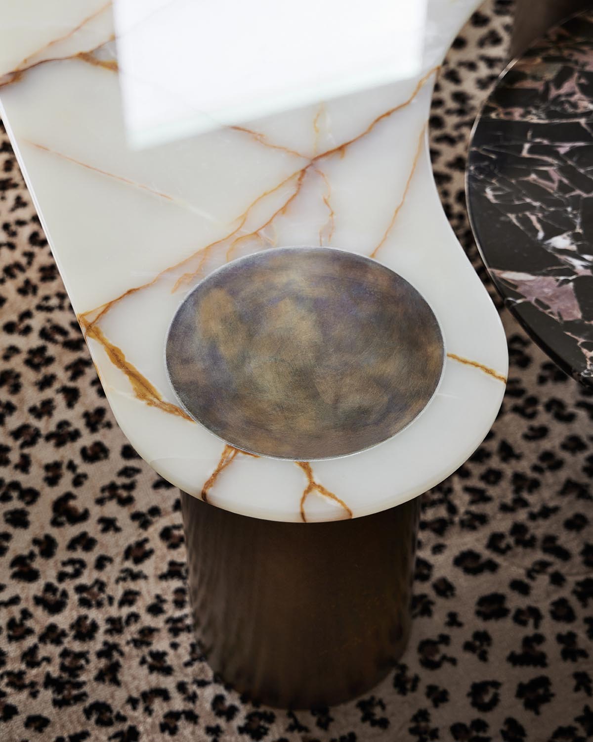Close-up of white marble table with gold veining, featuring a round worn metallic bowl inset, standing on a textured cylindrical base.
