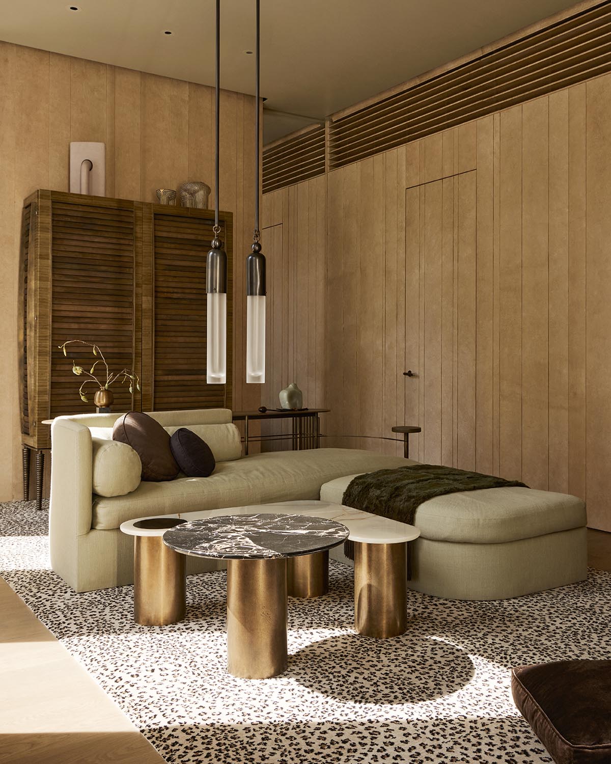 Minimalist living room with beige sectional sofa, round marble and brass coffee tables, wooden cabinet, and leopard print rug