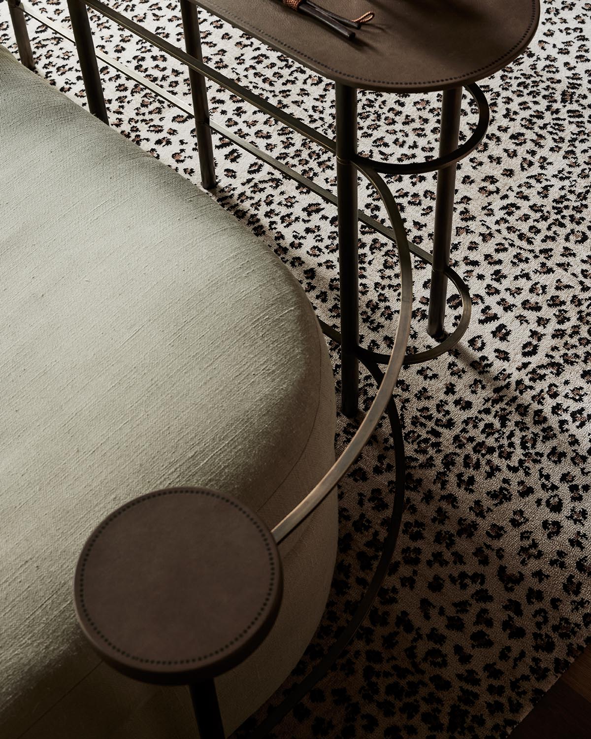 Close-up of curved metal side table with leather surfaces positioned next to pale textured sofa on patterned rug