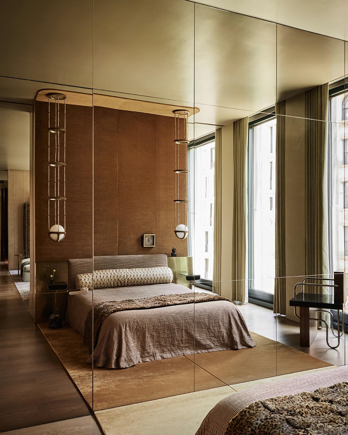 Modern bedroom with a brown textured accent wall, low bed with patterned pillows, and large floor-to-ceiling windows with curtains