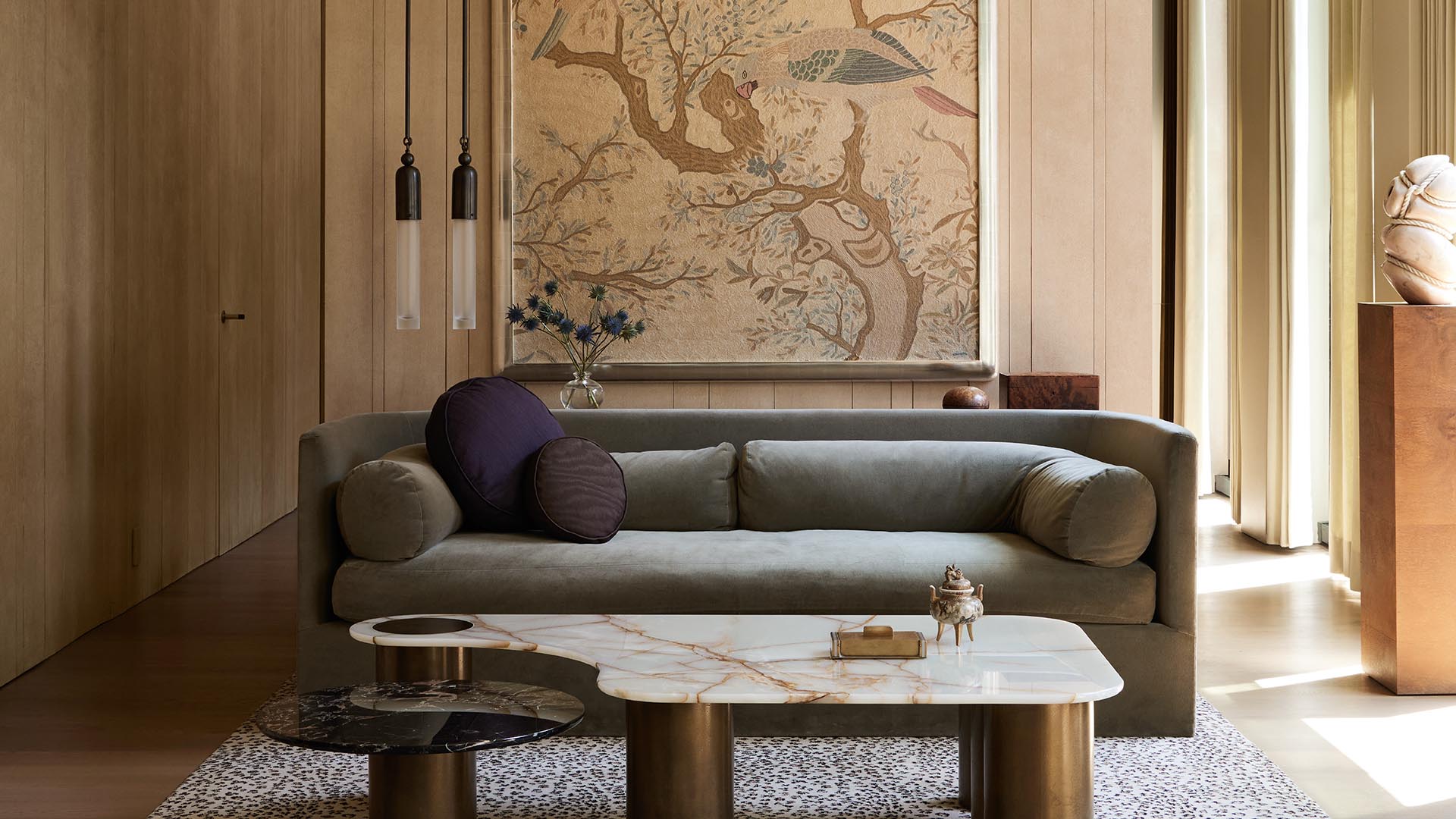 Minimalist living room with gray sofa, two round marble coffee tables, and botanical wall art in warm natural light
