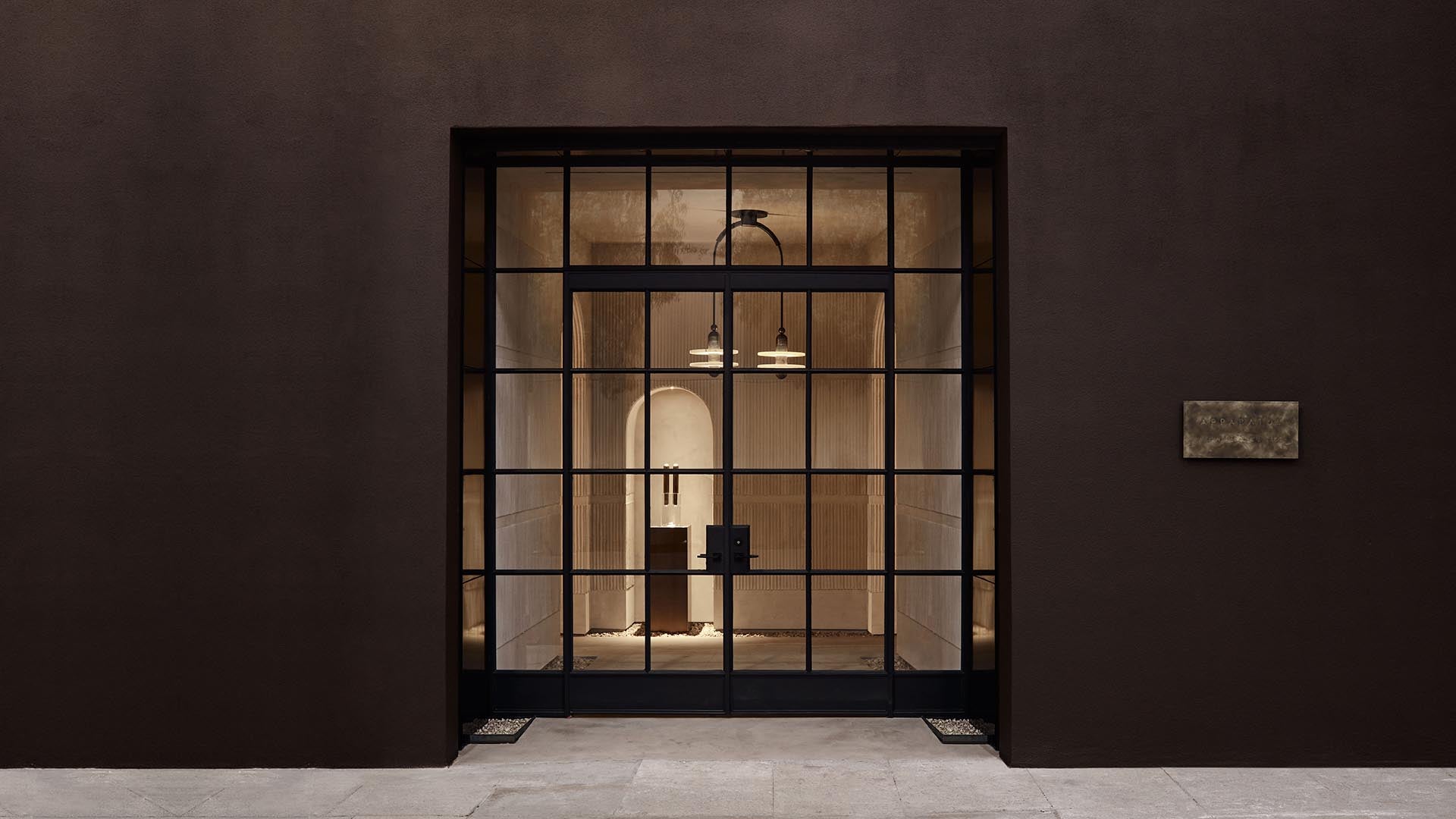 Minimalist interior with arched doorway and pendant lights seen through large black-framed glass doors in dark wall