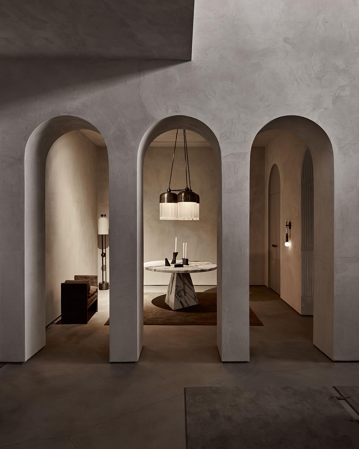 Interior view of a modern space featuring three arched openings, a marble round table with pendant lights, and muted earth tones