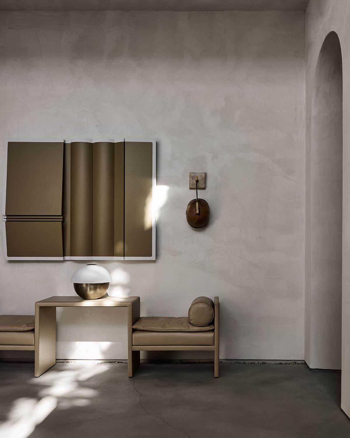 Minimalist room with beige built-in bench seating, a simple table, abstract wall art, and soft natural light on textured wall.