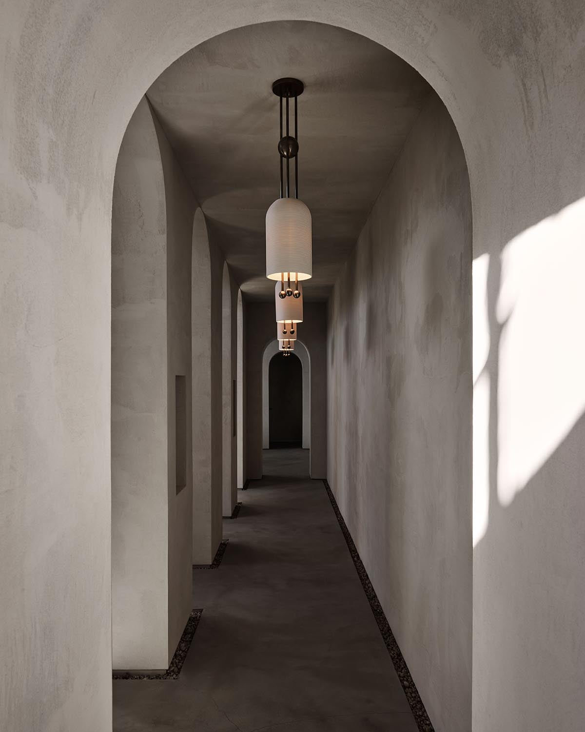 Narrow hallway with smooth plaster walls, arched ceilings, and cylindrical pendant lights casting soft shadows.