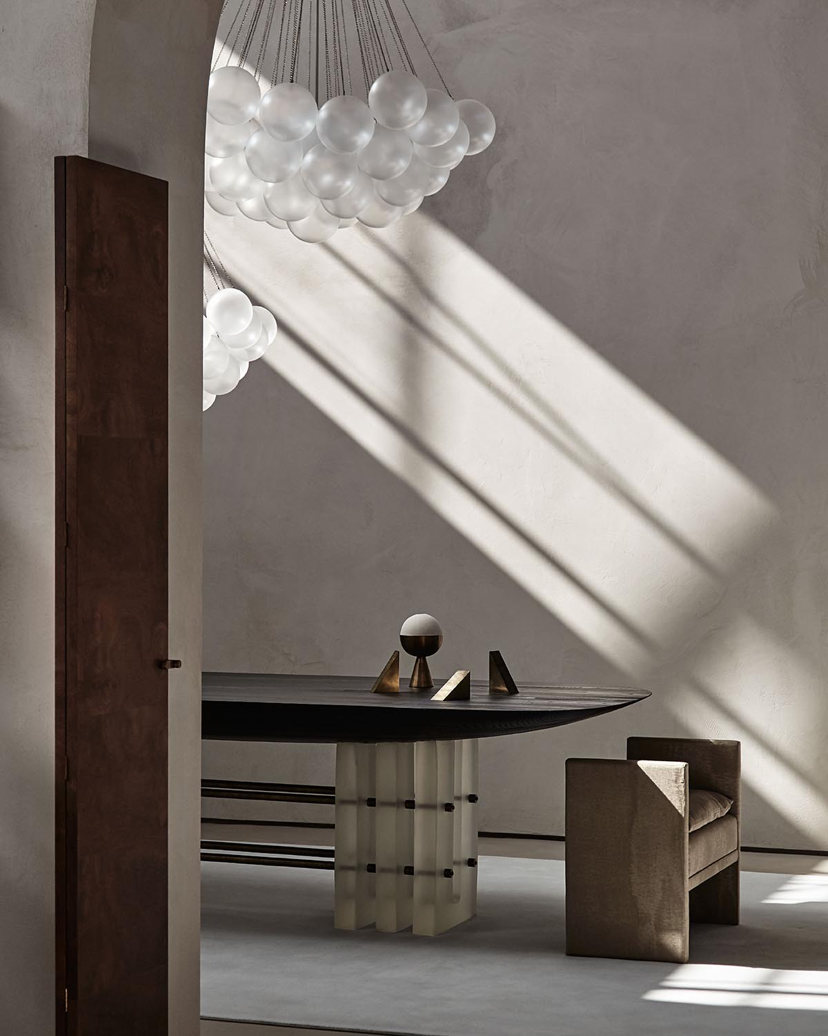Minimalist interior with a sculptural black table, geometric decor, upholstered chair, and cluster of spherical pendant lights