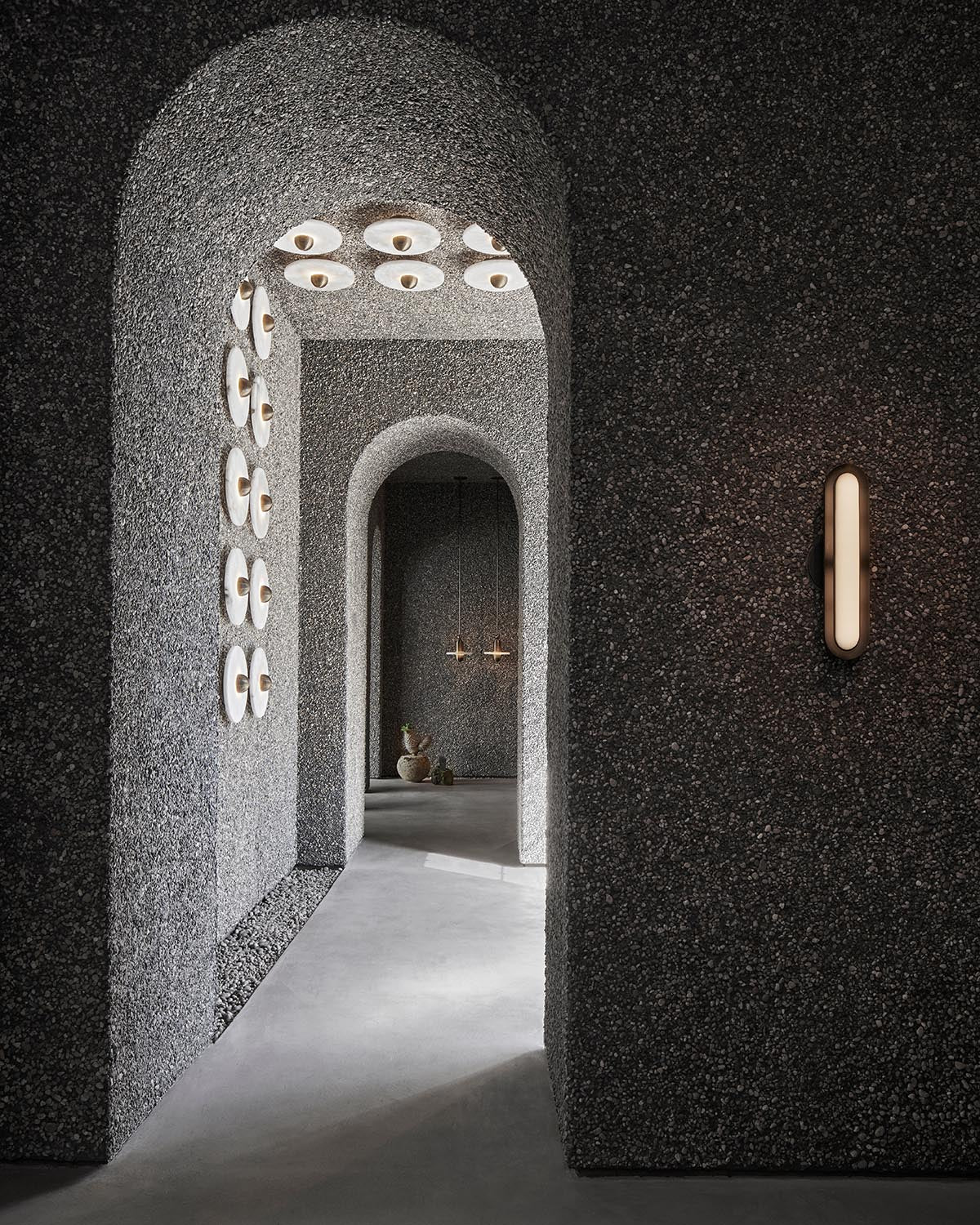 Textured gray arched corridor with circular wall lights and pendant lamps in minimalistic interior space