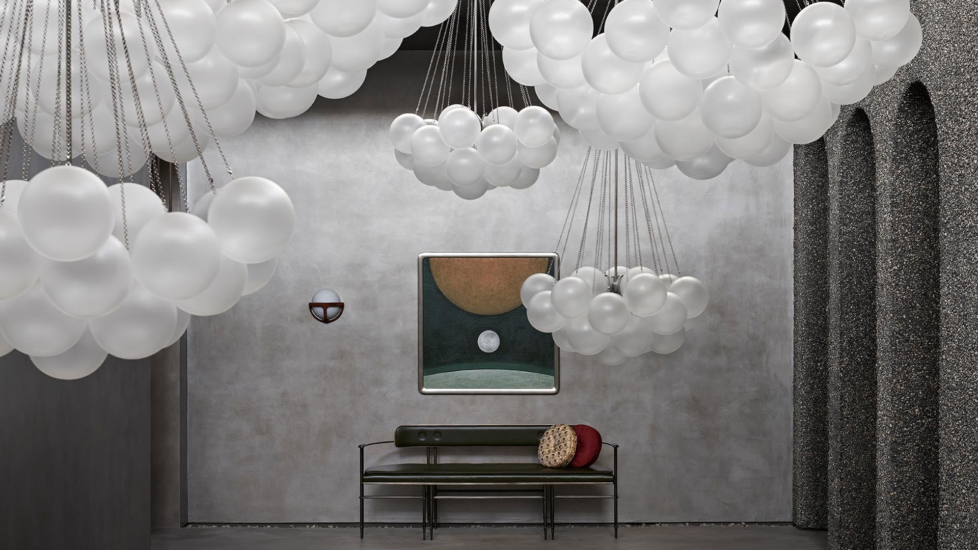 Minimalist interior with hanging white cluster lights, modern bench, and abstract wall art on a textured gray wall backdrop