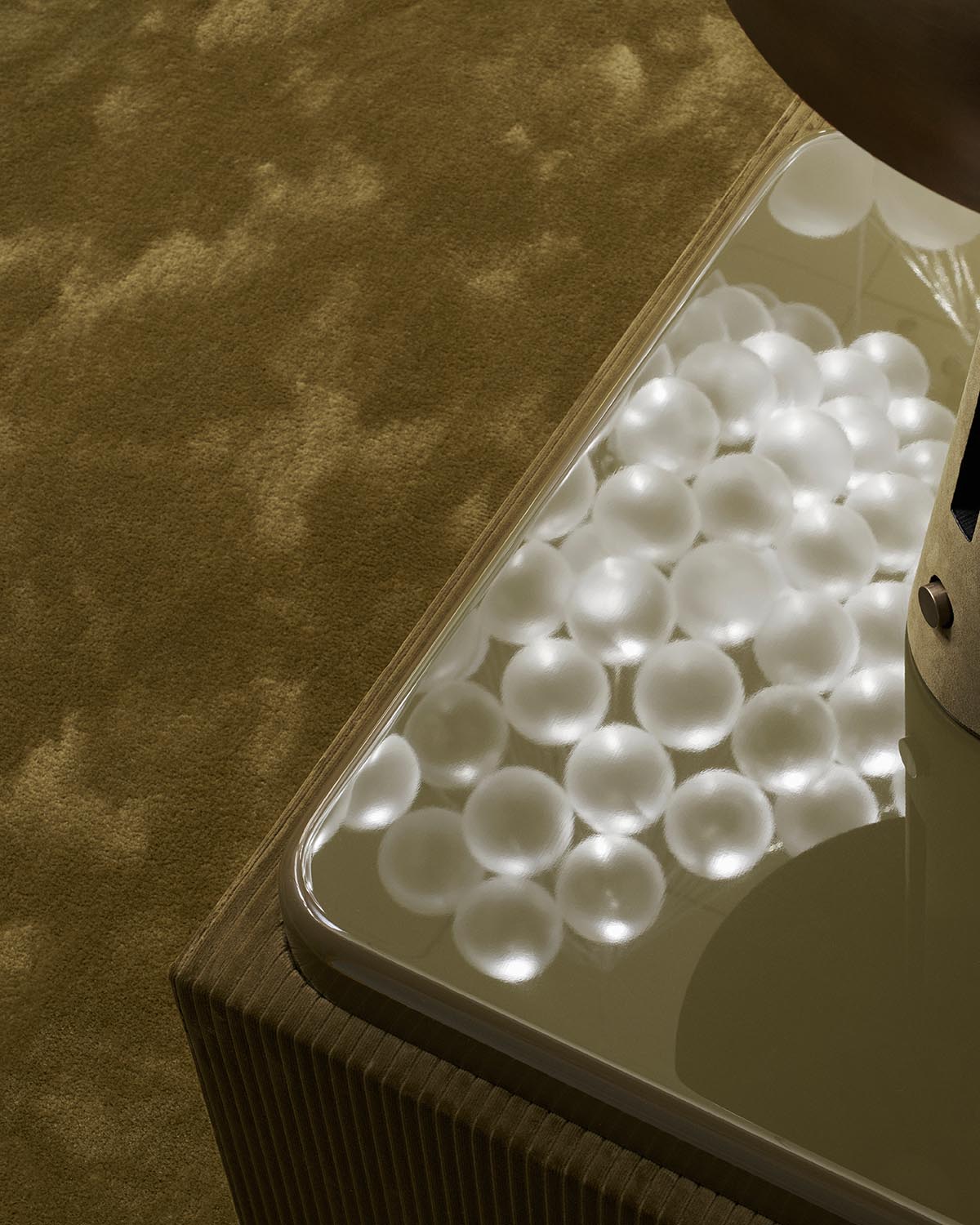 Close-up of a reflective glass surface on a wooden table showing clustered translucent spheres and soft shadow patterns on a textured backdrop