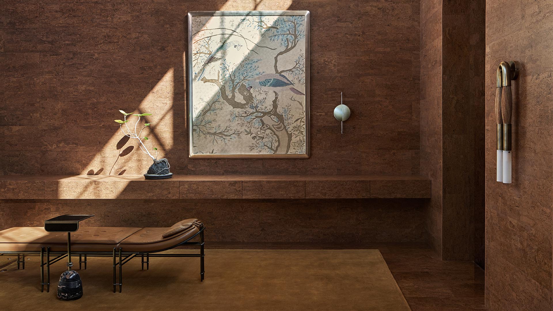 Minimalist interior with textured brown walls, a bench with cushions, abstract wall art, and decorative hanging objects.