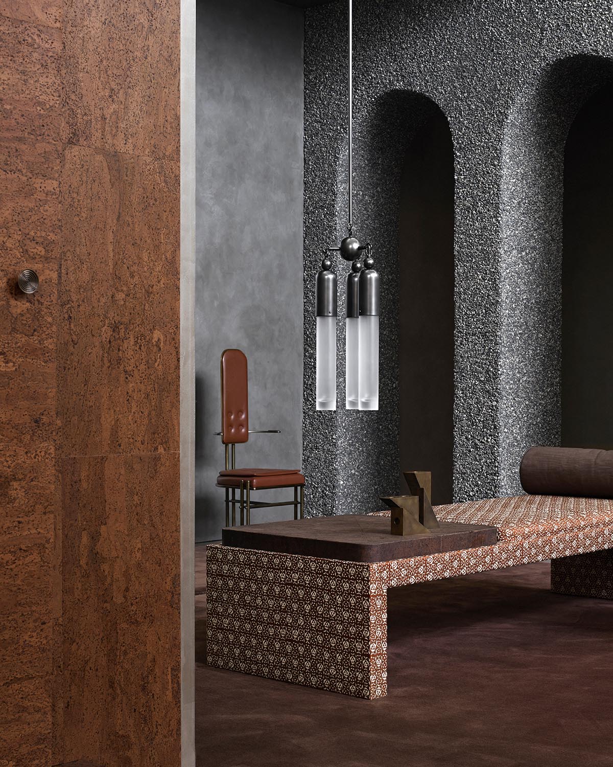 Interior space with textured gray arched walls, a patterned bench, leather chair, and hanging cylindrical pendant lights