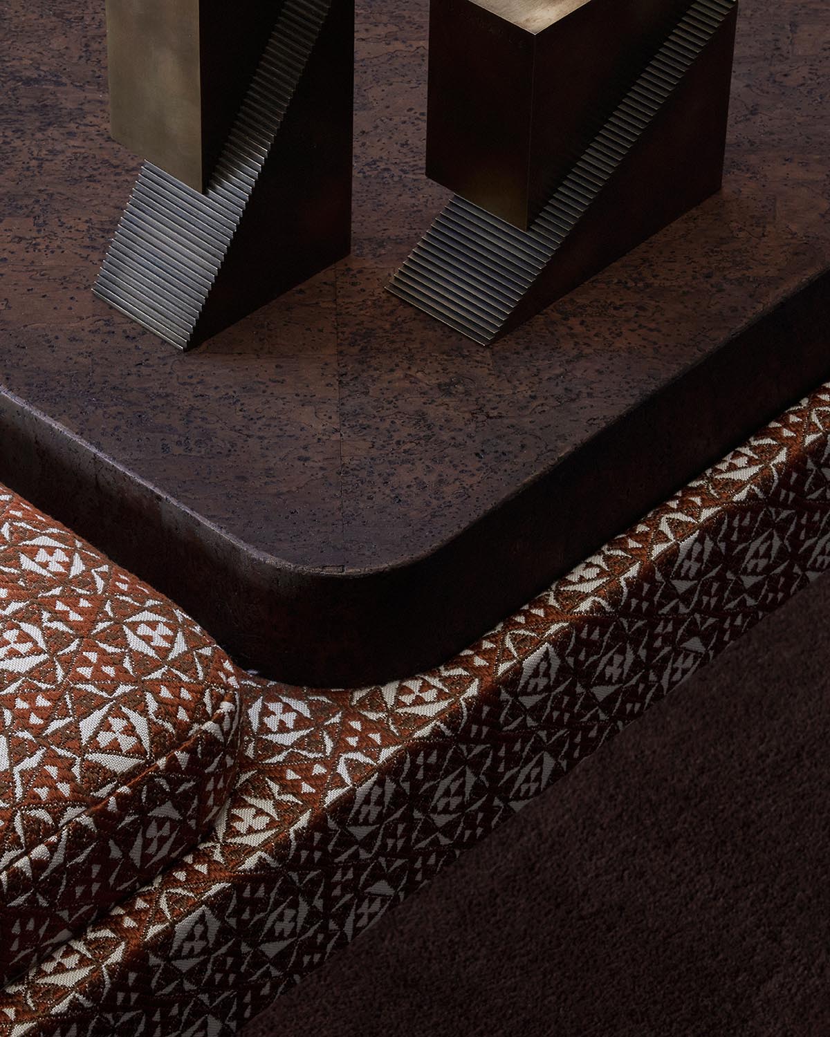 Close-up of dark brown textured surface with geometric bronze sculptures and patterned fabric edge below