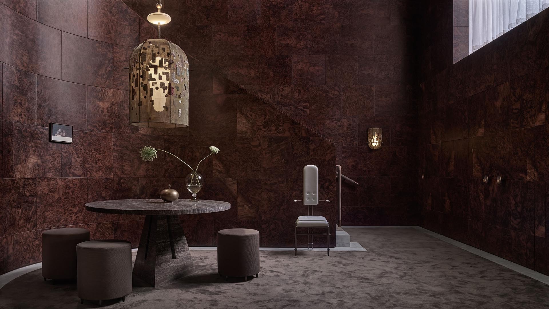 Contemporary room with dark textured walls, round stone table, cylindrical stools, and a unique pendant light fixture