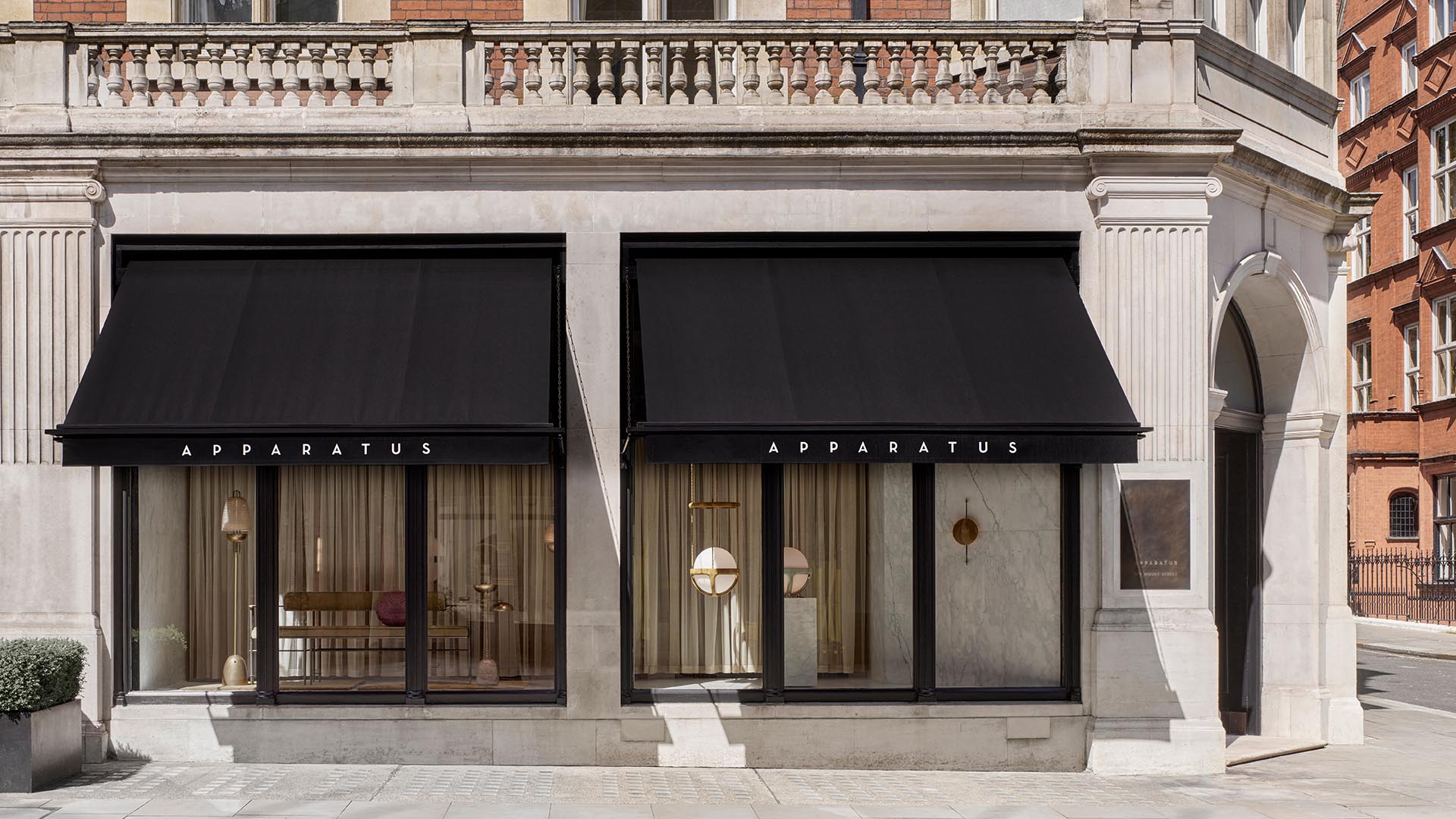 Exterior view of a corner building with black fabric awnings over large glass windows displaying modern interior lighting fixtures.