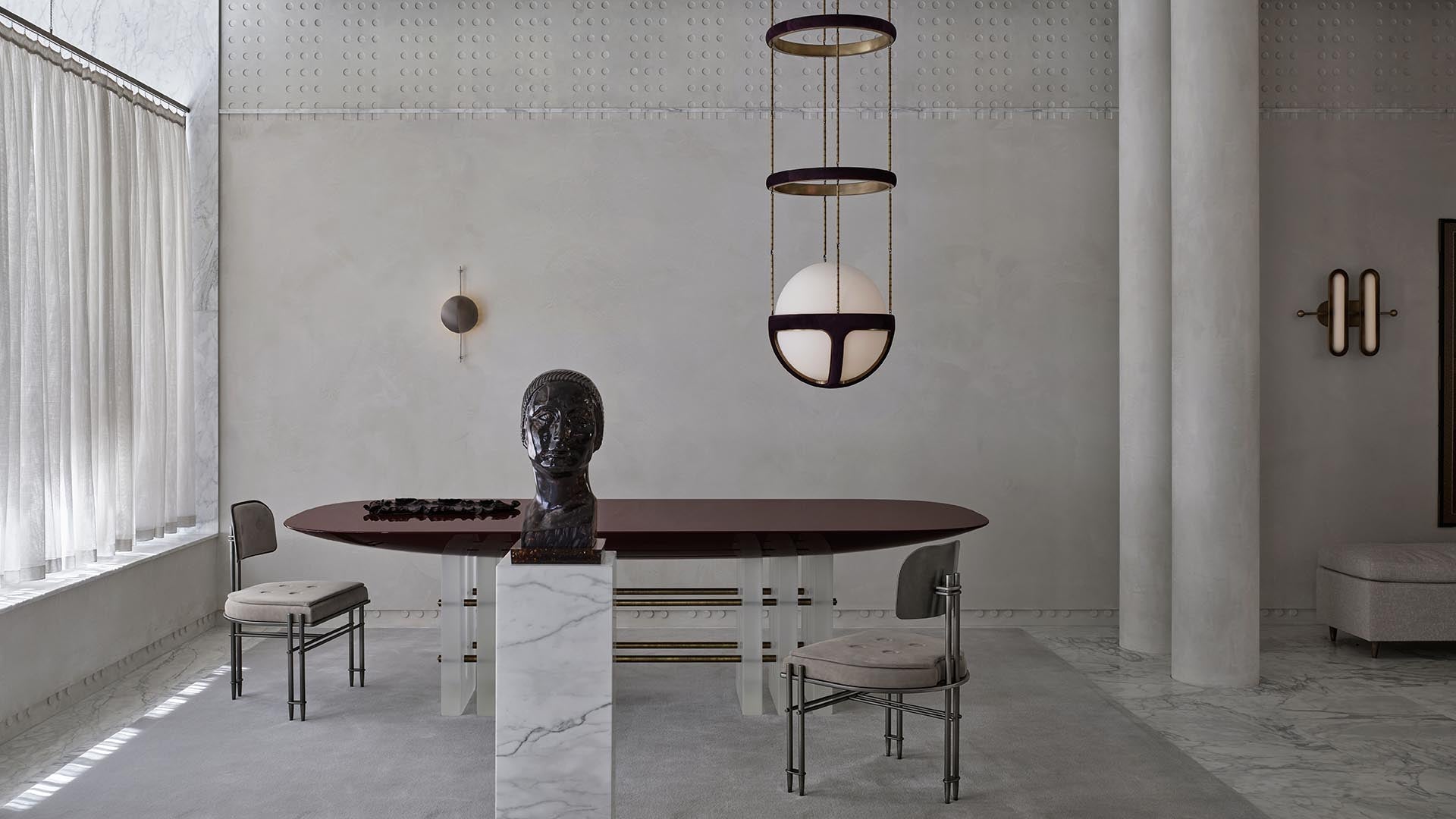 Minimalist dining room with dark oval table, sculptural bust on marble pedestal, two chairs, and pendant light fixture