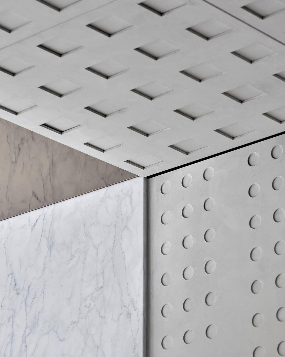 Close-up of geometric architectural detail featuring marble and textured concrete panels with raised circular and square patterns