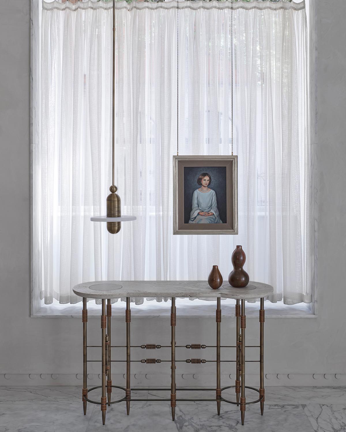 Minimalist interior with sheer white curtains, an oval table with spindle legs, hanging pendant light, framed portrait, and ceramic vases