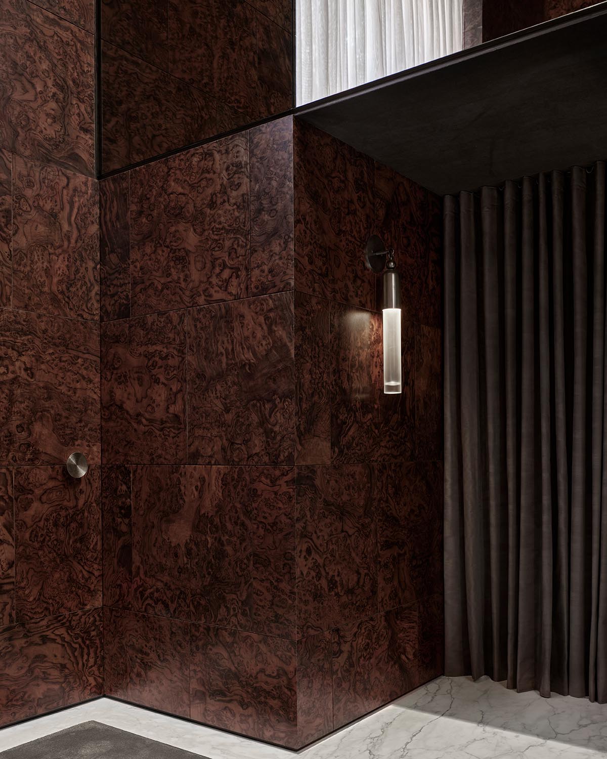 Dark brown marbled wall panels with a vertical cylindrical light fixture beside closed dark grey floor-length curtains
