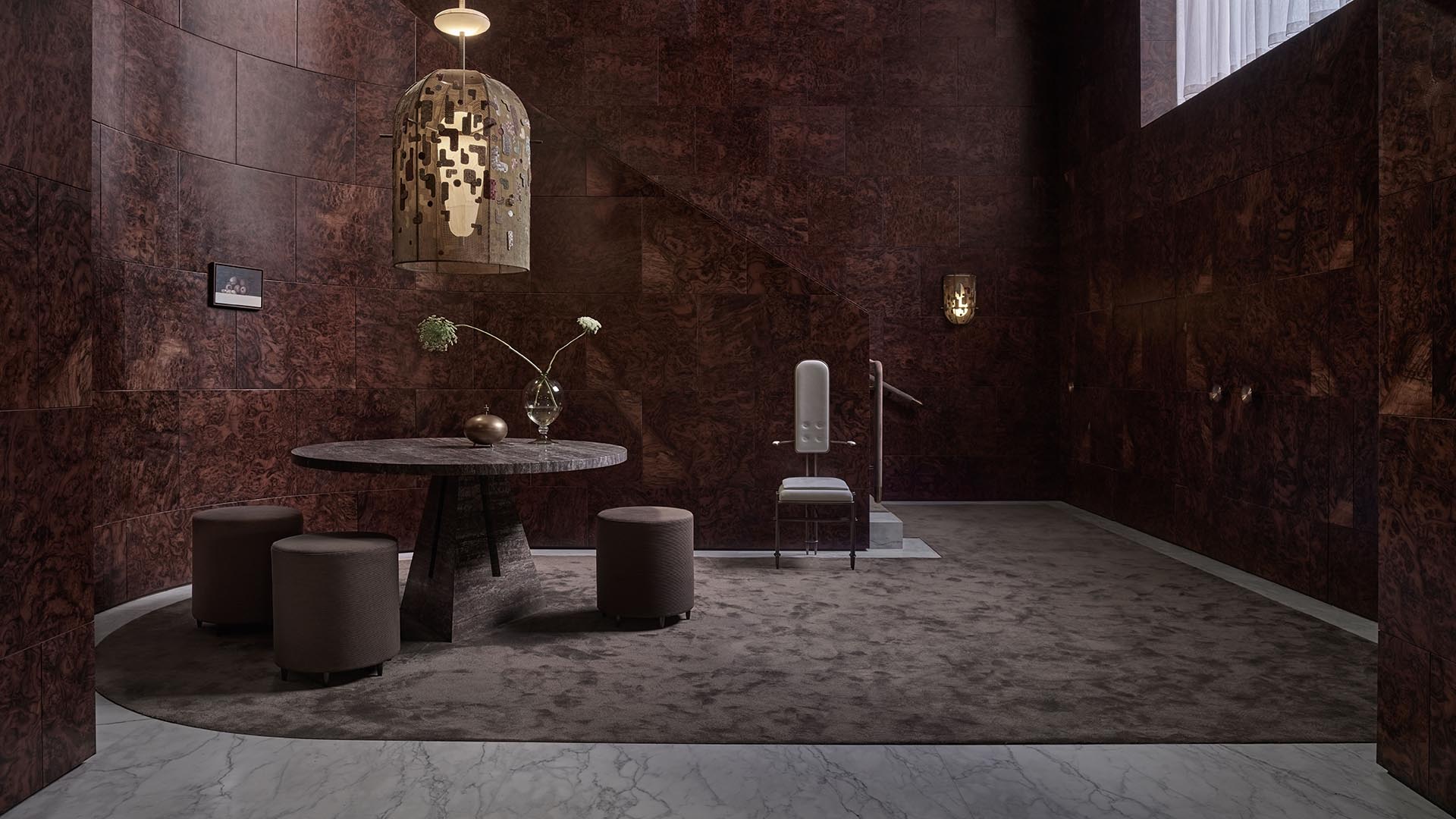 Dimly lit room with dark textured walls, circular marble table, four cylindrical stools, and a modern spotlight fixture