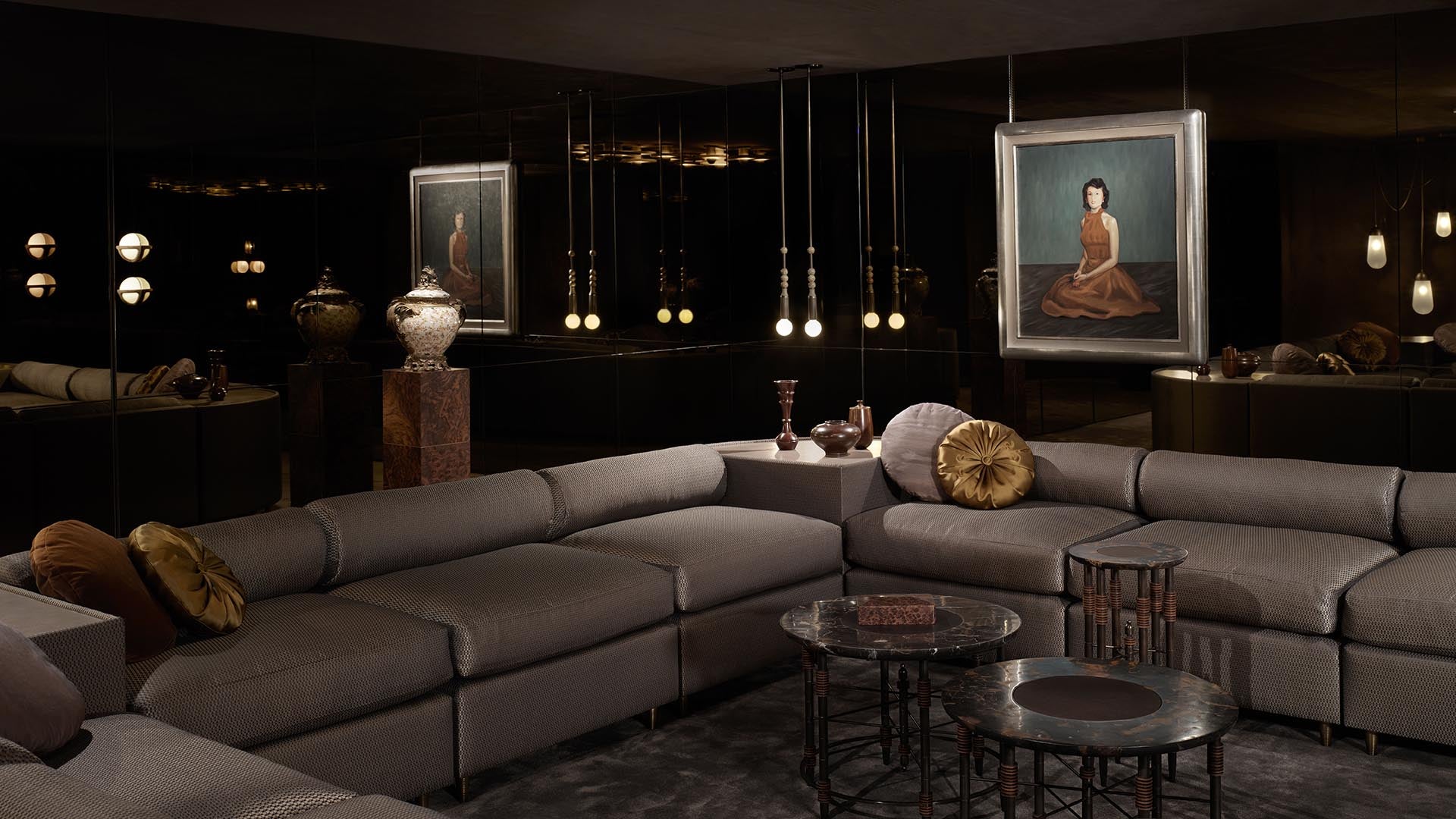 Dark modern living room with large gray sectional sofa, round black metal coffee tables, and framed portraits on walls