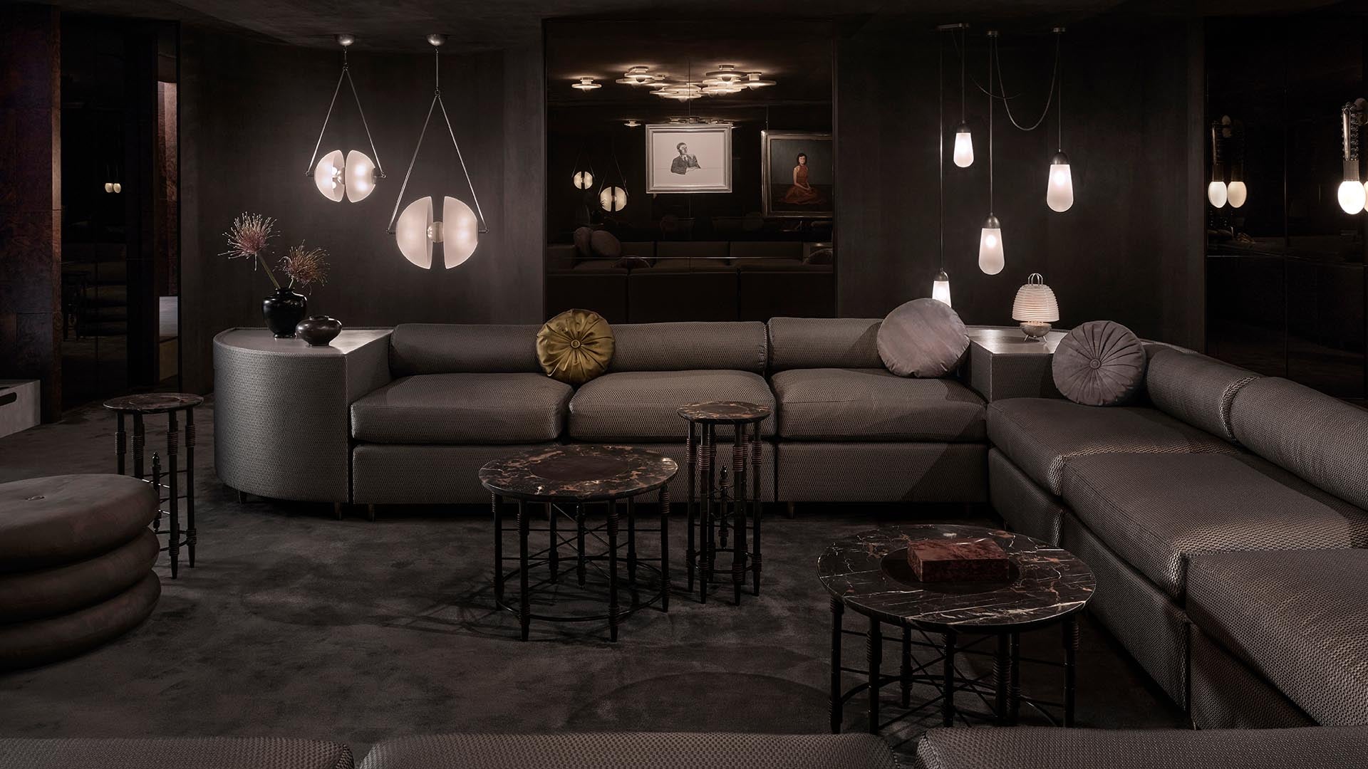Dimly lit modern lounge with dark leather sectional sofa, round marble coffee tables, and hanging pendant lights